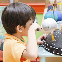Elementary-age child looking at a planet through a magnifying glass in a classroom.